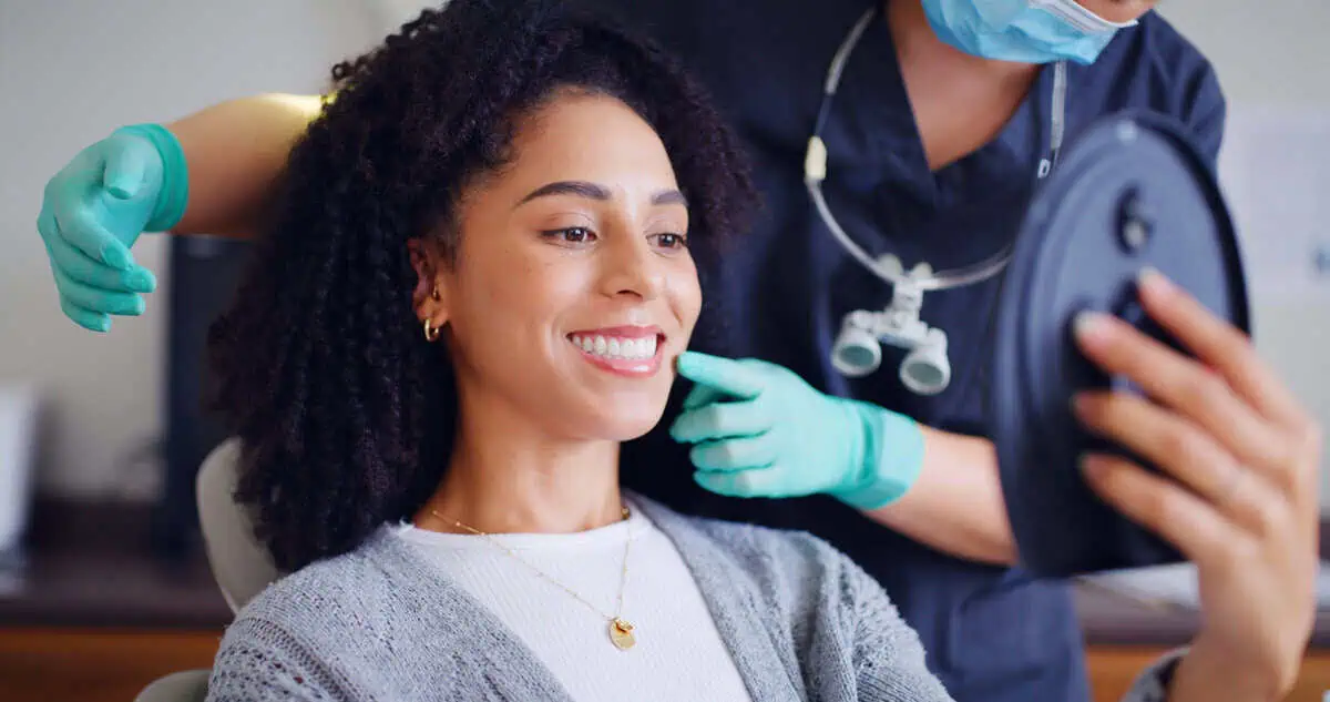 Smiling woman checking her teeth in a hand mirror at a dental visit