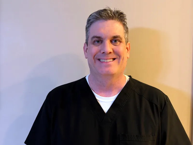 Dr. Devin Croft, orthodontist, smiling in navy scrubs